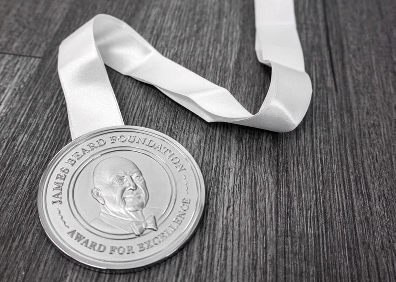 Silver James Beard chef award medal on white ribbon