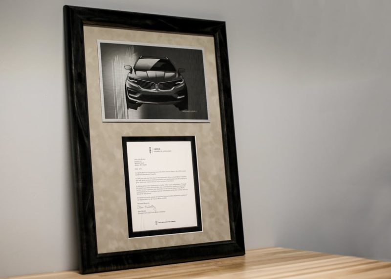 Framed document and metal plate with car image printed on it.